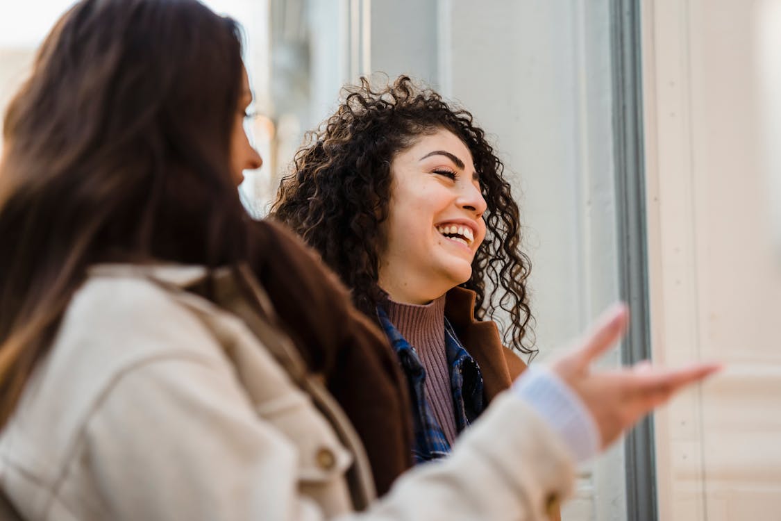 Two young women laughing together on a street, the kind of close friendship where funny roast-style birthday wishes are always well received