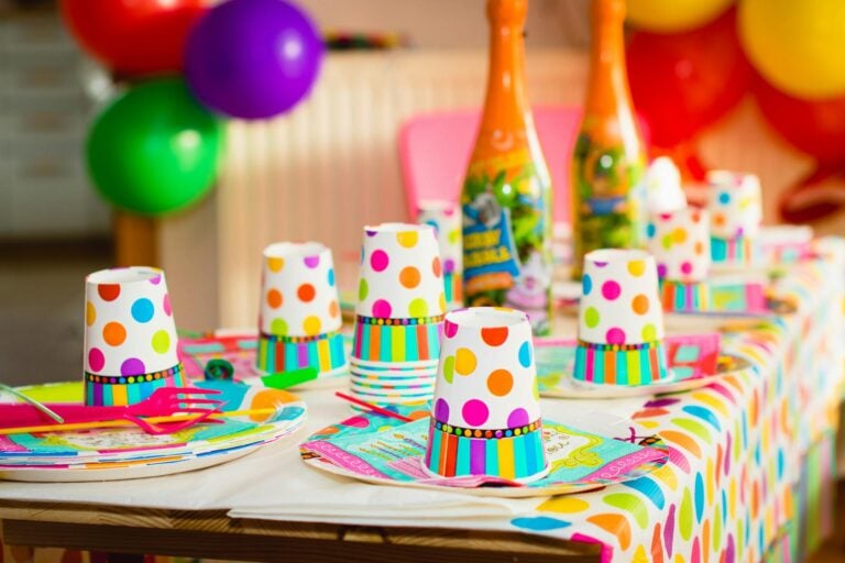 Colourful birthday party supplies including polka dot cups, balloons and tableware arranged on a party table
