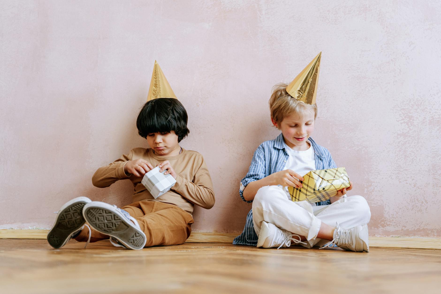 two boys in party hats opening birthday presents at an indoor birthday celebration