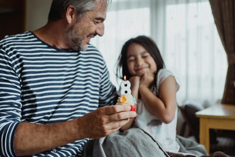 A joyful father and daughter celebrating her birthday indoors, blowing out candles together