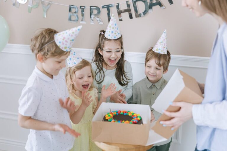 Children in party hats celebrating a birthday with a colourful cake indoors