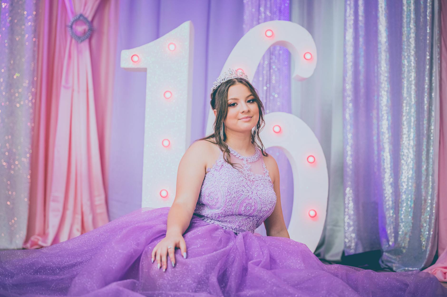 Teen girl in purple gown at an elegant Sweet 16 celebration with illuminated number 16 backdrop