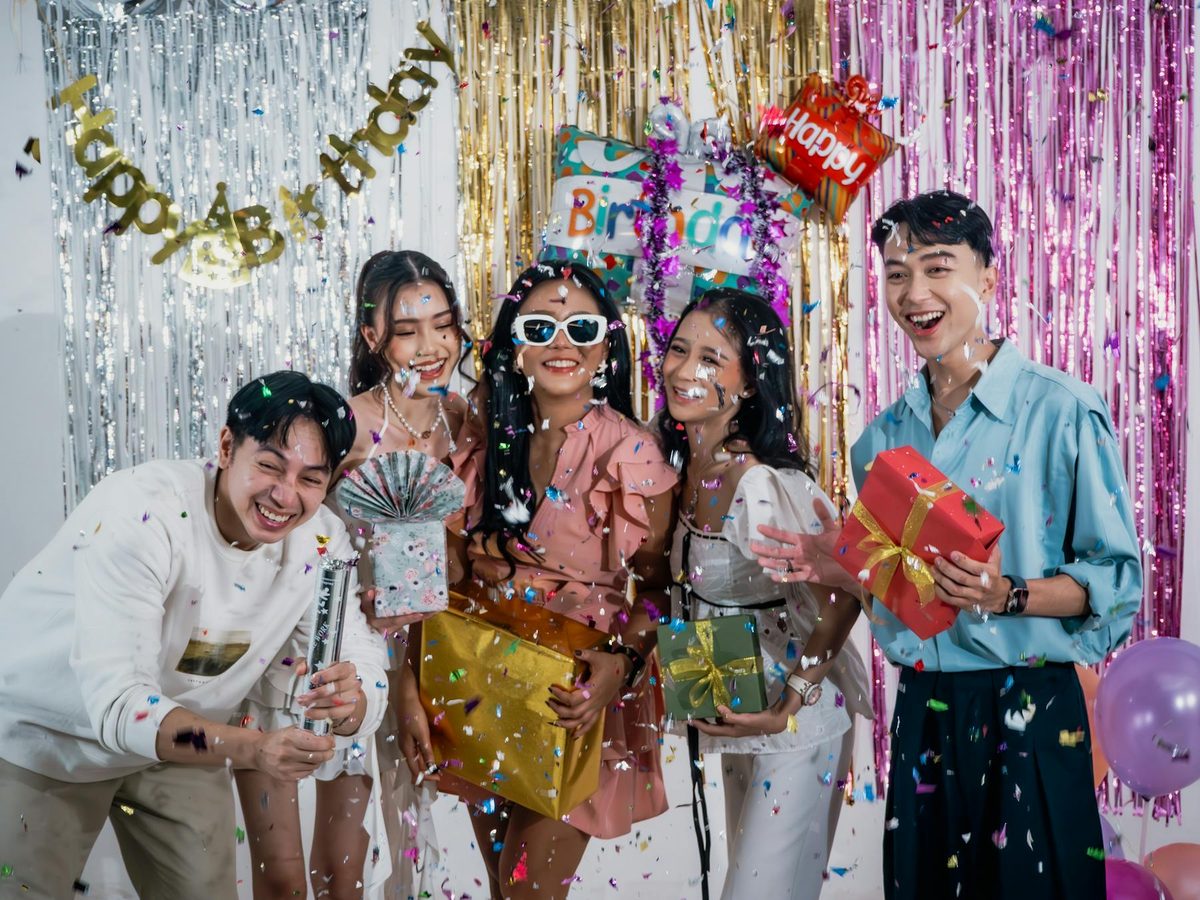 Young adults joyfully celebrating a birthday indoors with gifts and decorations, showing group experience gift ideas for 18th birthdays