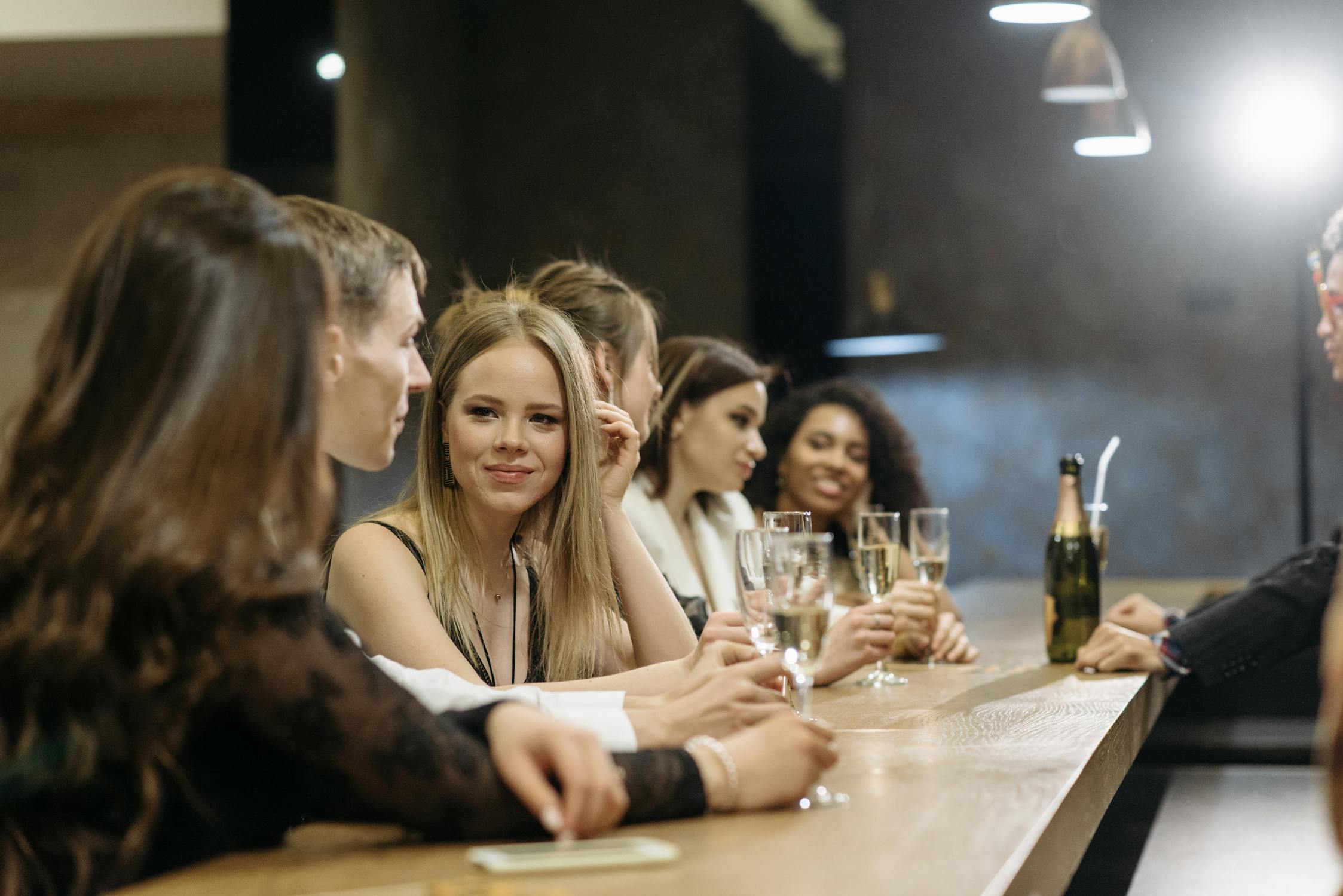 Diverse group of friends celebrating an 18th birthday night out with champagne at a bar