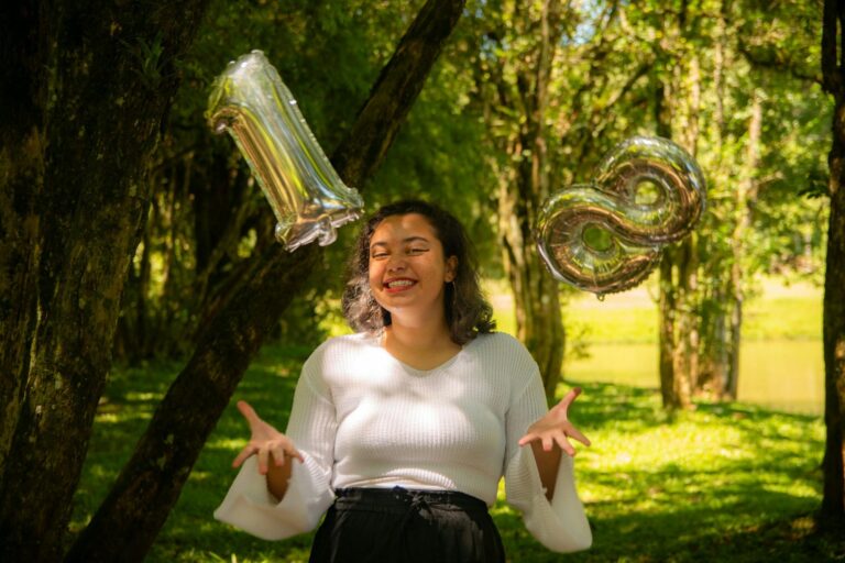 Young woman celebrating her 18th birthday outdoors with metallic number balloons, smiling at camera