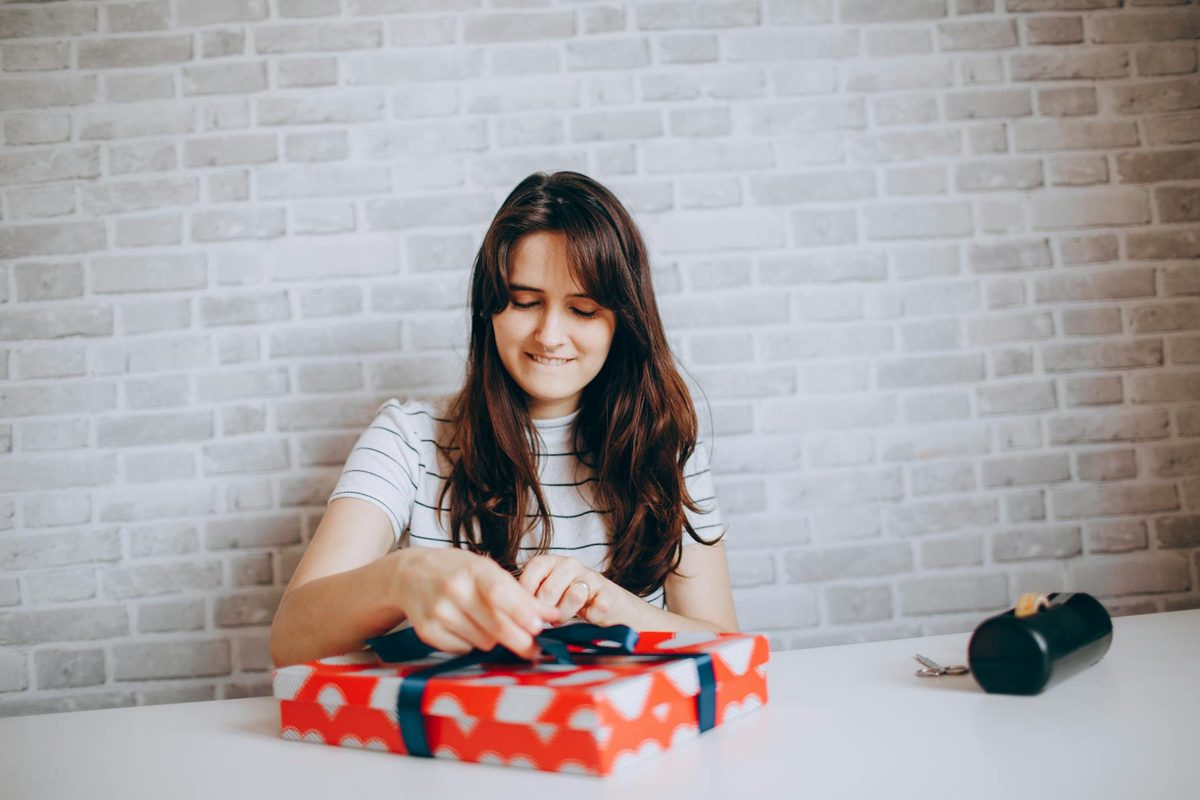 Young woman smiling as she opens a beautifully wrapped red gift box, ideal 18th birthday gift idea