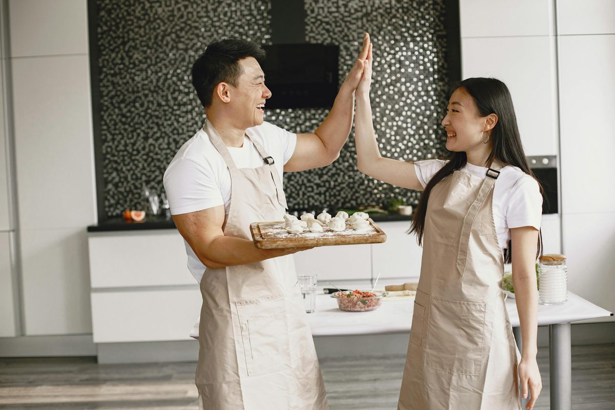 Couple sharing a high-five while making dumplings together in a cooking class, a popular 40th birthday experience gift idea