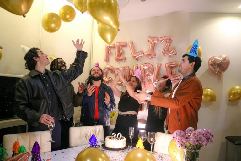 Group of friends in their 40s celebrating a milestone birthday indoors with balloons, cake and champagne