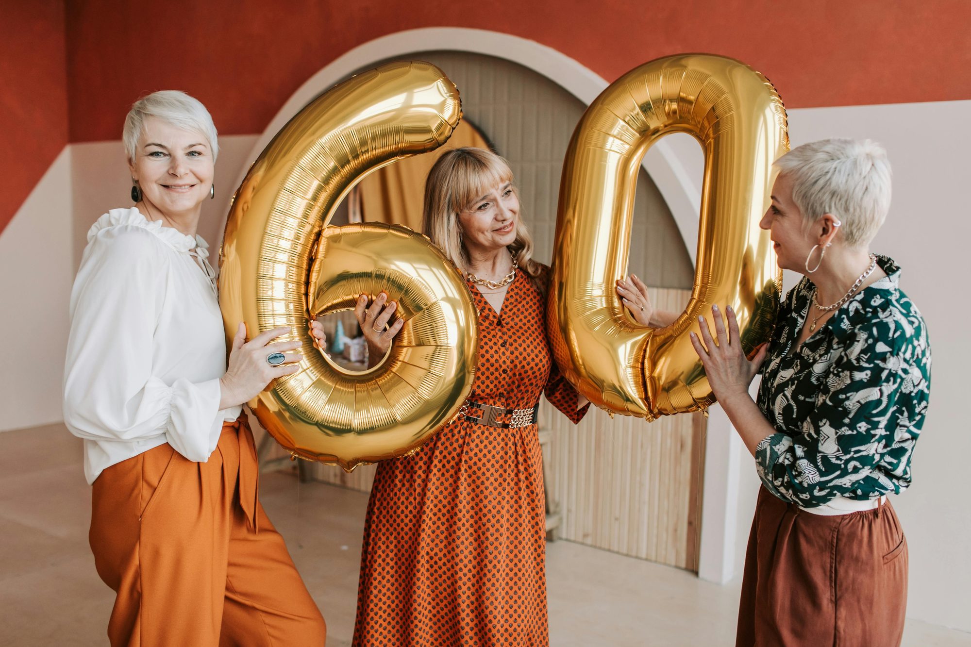 Two women in their sixties holding gold number balloons and laughing at a 60th birthday party celebration