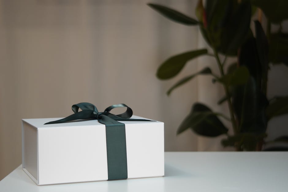 A neatly wrapped white gift box with dark ribbon on a clean table, understated and professional, suitable for a workplace birthday gift