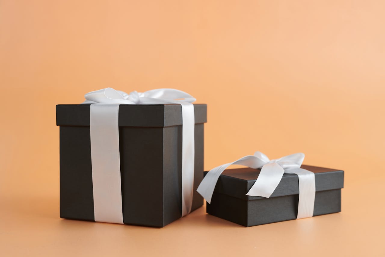 Two elegant black gift boxes with white ribbons, representing birthday gift ideas for him