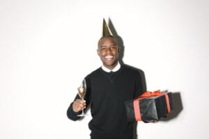 Smiling man with champagne glass and birthday gift, celebrating his birthday