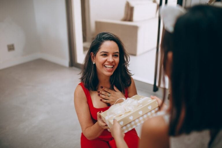 A happy woman receives a birthday gift from her daughter indoors, capturing a warm moment of joy and connection