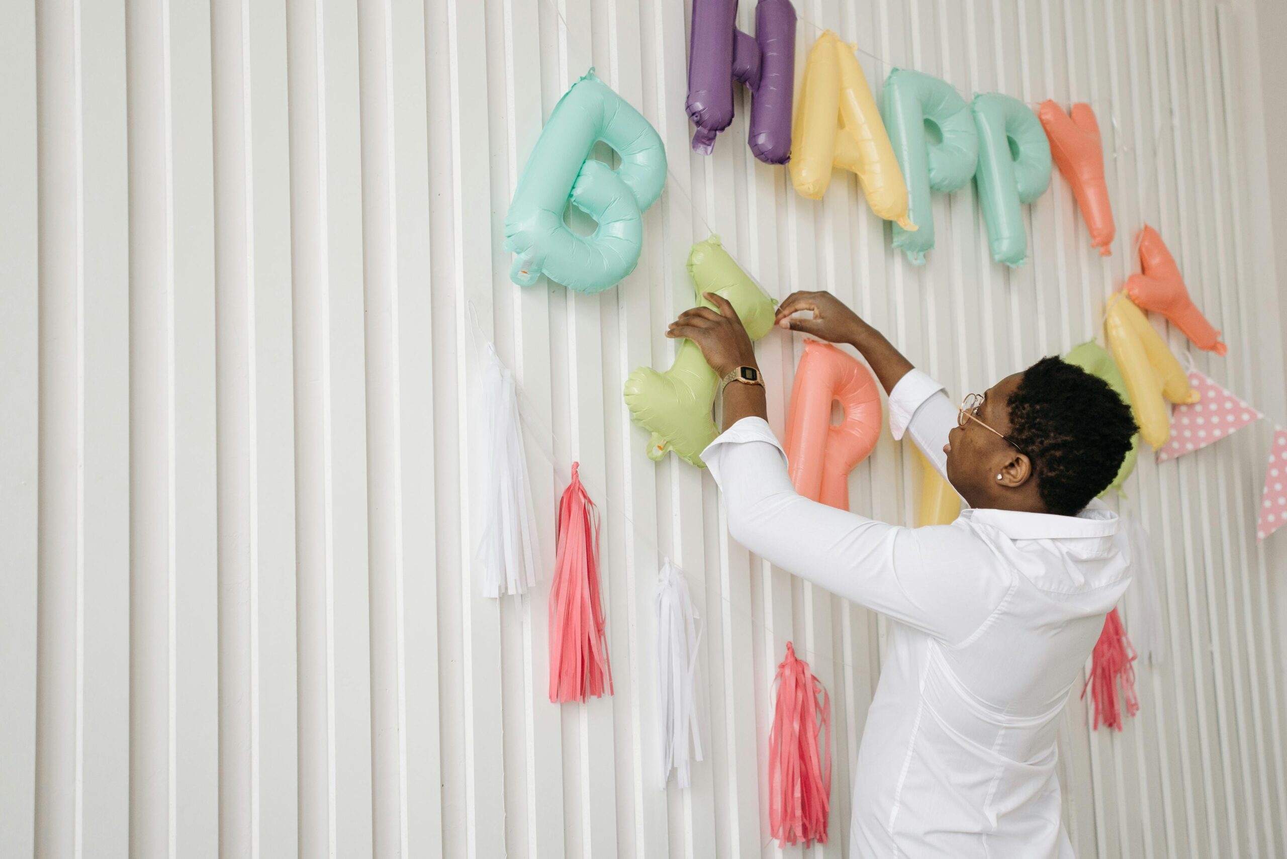 Man setting up colourful balloon decorations for a surprise birthday party indoors