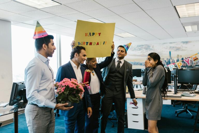 Colleagues celebrating a birthday in a modern office setting with festive decorations and balloons