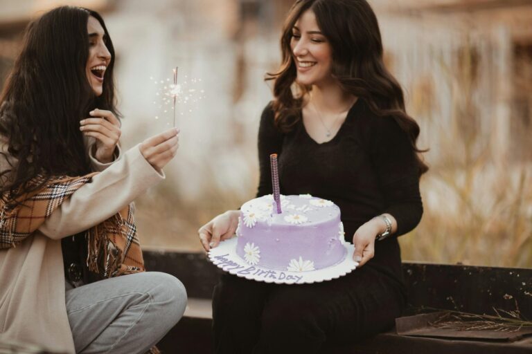 Two women celebrating a birthday outdoors with cake and sparklers, representing a heartfelt sister birthday celebration