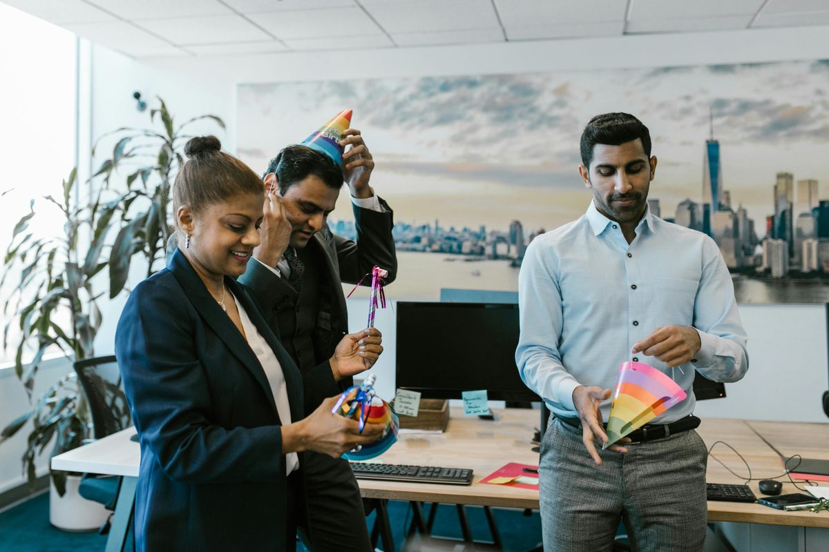 Three workplace colleagues smiling and celebrating a birthday together in an office with party hats
