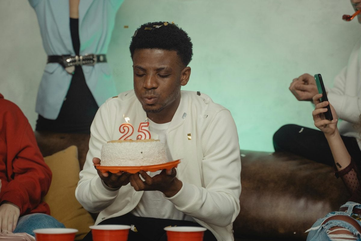 Young adult man blowing out candles on a birthday cake at a milestone birthday celebration