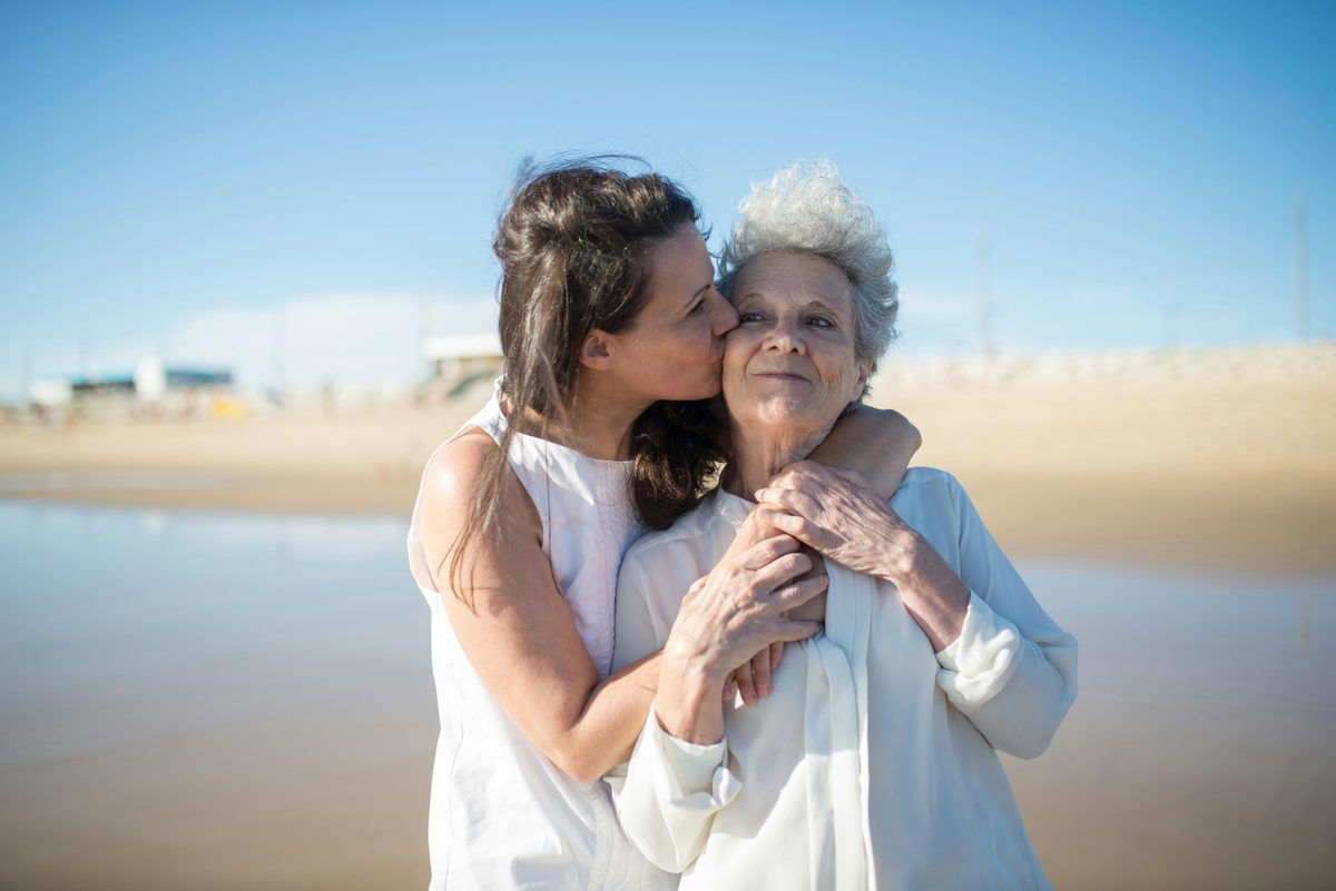 Adult daughter kissing her mother on the cheek at a birthday celebration, warm sunny setting