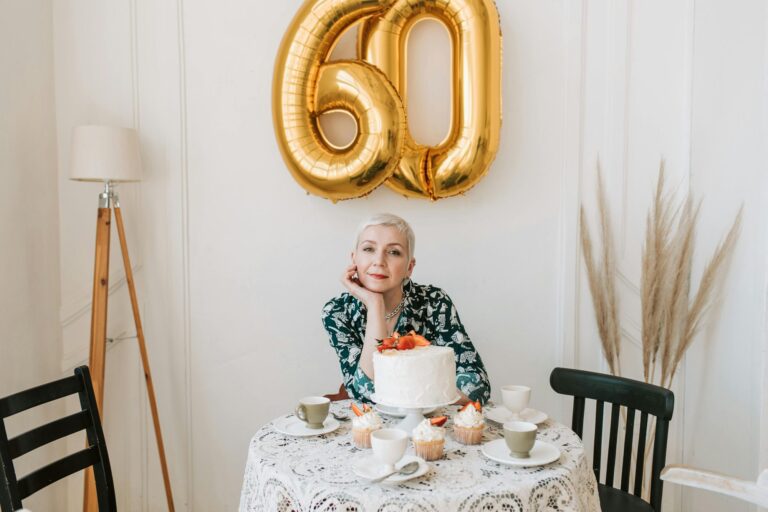 Senior woman celebrating 60th birthday with cake and balloons, warmly smiling at her birthday party