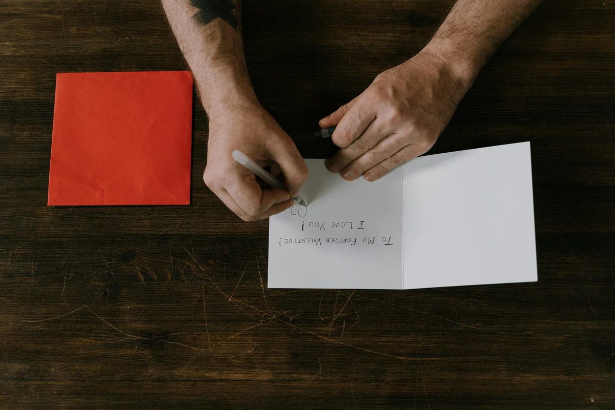 Man writing a romantic birthday message on a card with a red envelope, top-down view