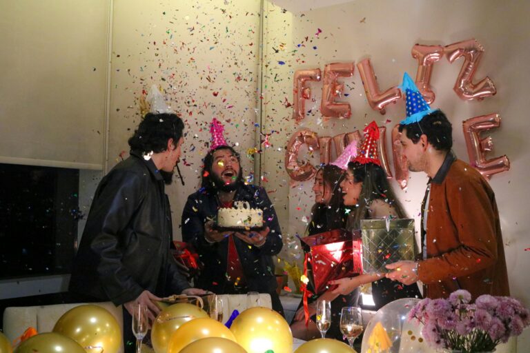 Adults cheering and celebrating at a surprise birthday party with cake, gifts, and confetti indoors